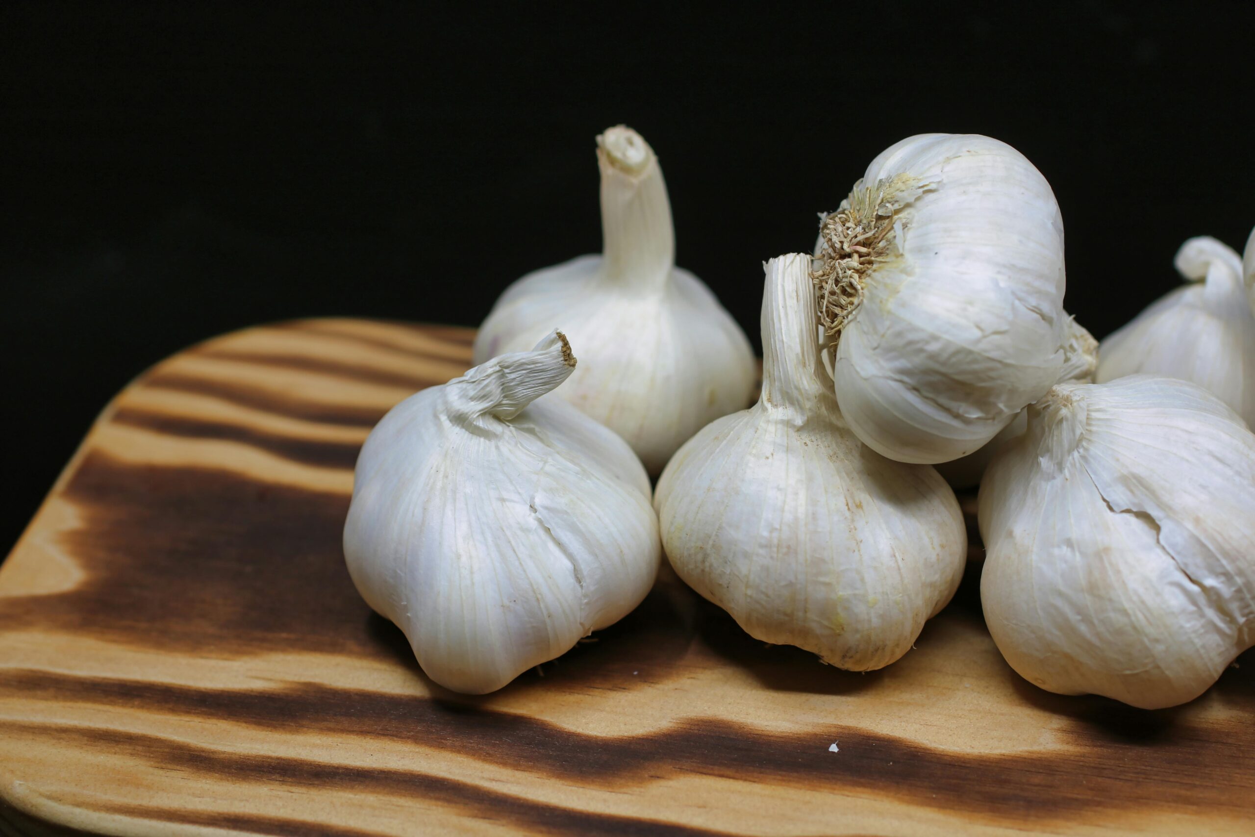 pexels photo 1392585 1392585 Fresh garlic bulbs placed on a wooden board with a black background, perfect for culinary themes.