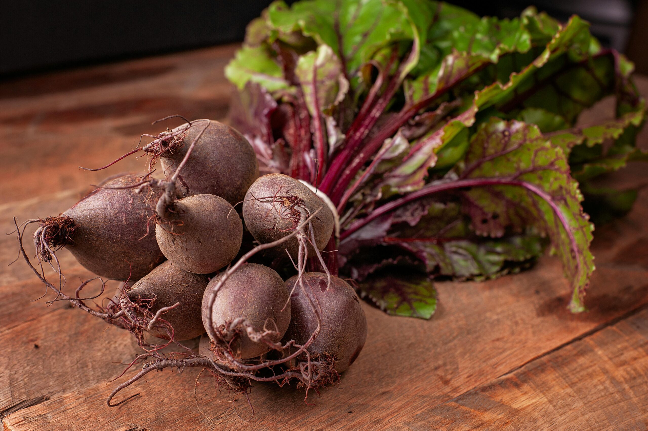 pexels photo 29436276 29436276 Bundle of fresh organic beetroots with vibrant green leaves on a wooden surface.