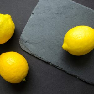 Home High-angle shot of vibrant lemons on dark slate, emphasizing freshness.